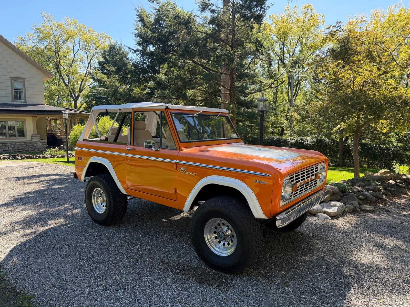 Orange 1974 Ford Bronco Sport with white bikini top on a gravel drive